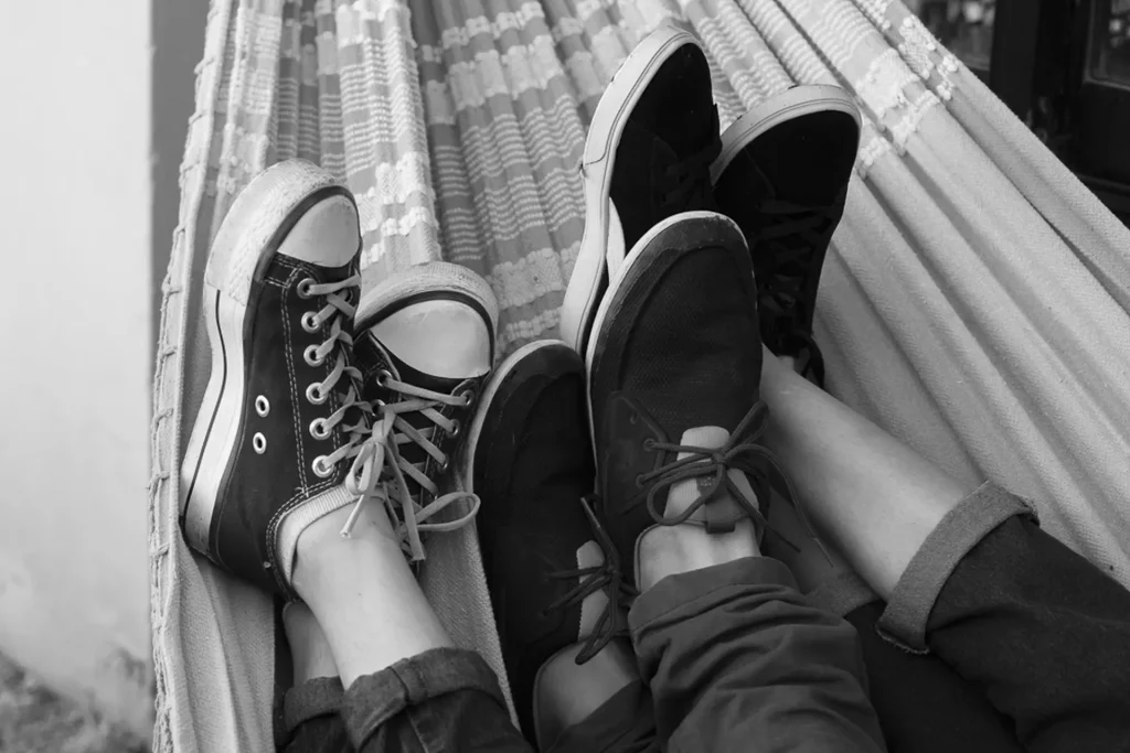3 pares de pies cruzados con zapatillas descansando juntos sobre una hamaca paraguaya